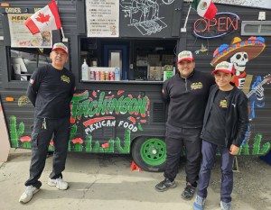 Three men stand in front of a Mexican themed food truck.