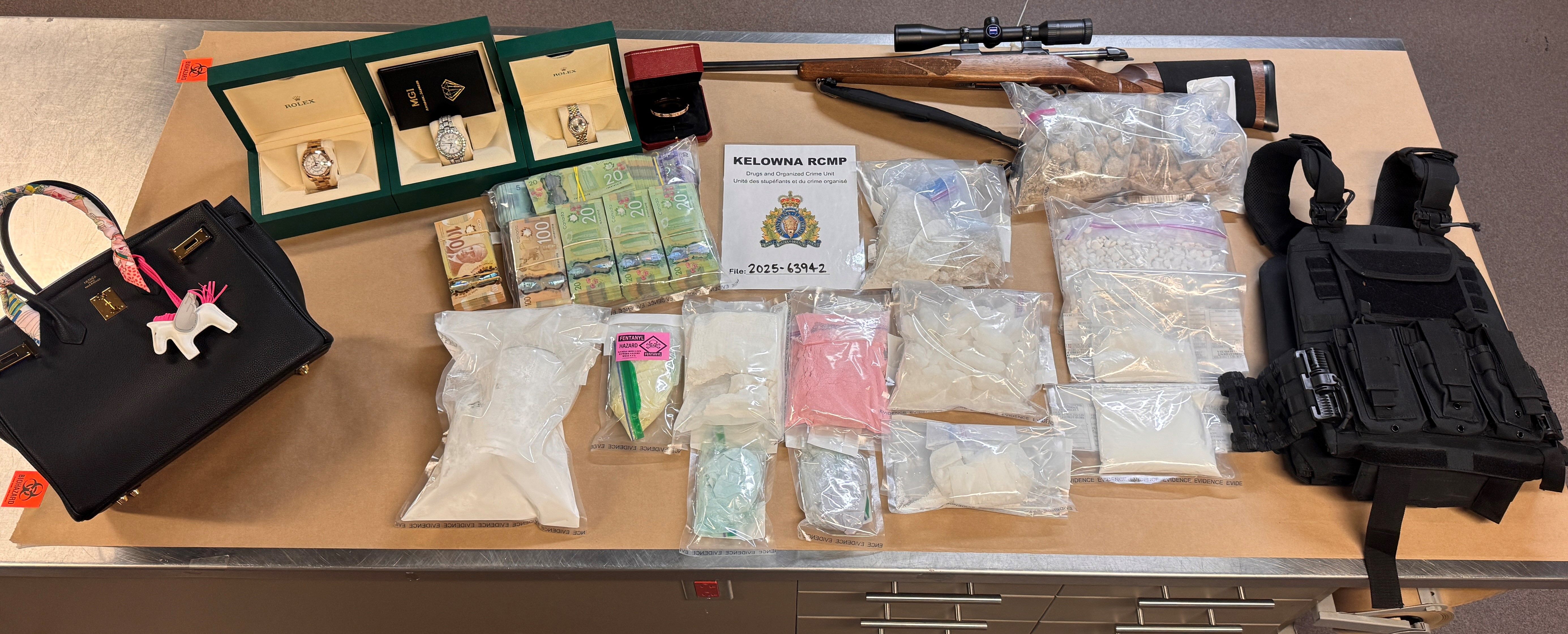 Drugs, cash, jewellery, a firearm, body armour and a rifle displayed on a table.