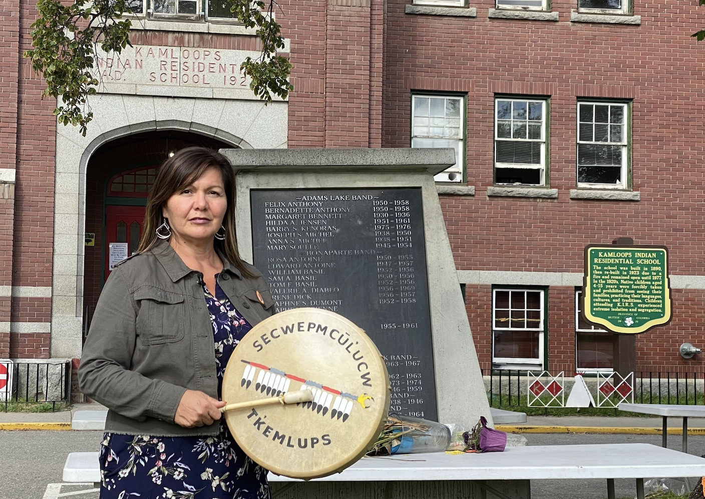 A woman holds a drum in front of a memorial monument.
