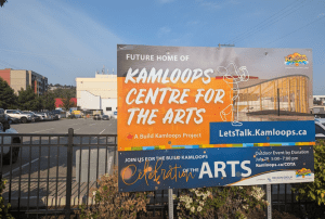 A billboard advertises an arts venue in front of a paved parking lot.
