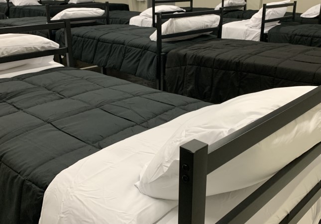 Rows of beds with blanks and pillows in a homeless shelter.