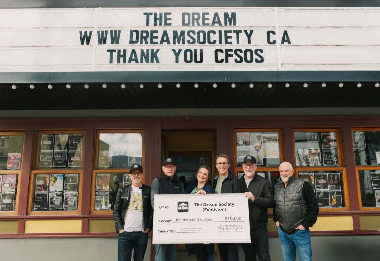 People holding a big cheque in front of the old Dream Cafe in Penticton.
