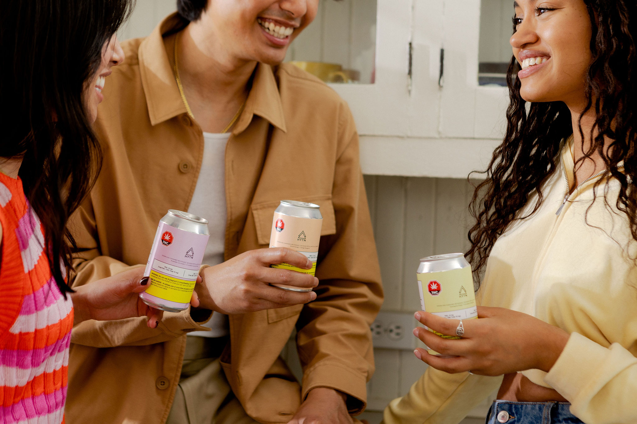 Three people holding cannabis infused canned drinks.