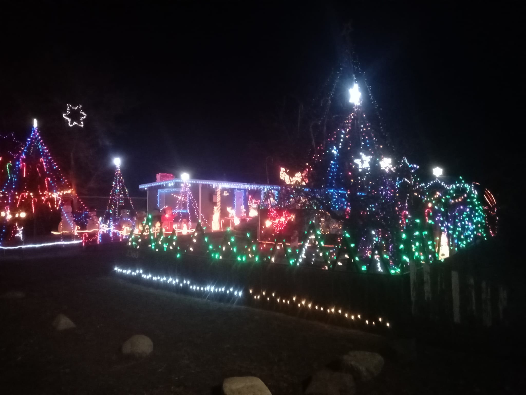 A residential home and property is glowing with Christmas lights at night.