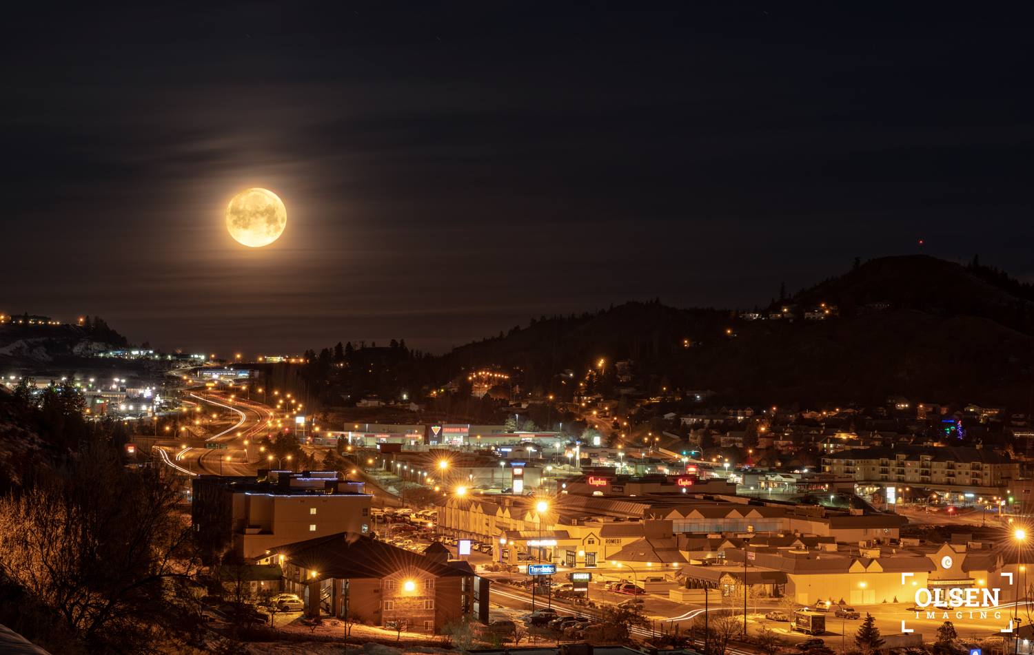 A full moon shines above a city bright with lights.