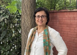 A woman smiles in front of a tree trunk and brick wall.