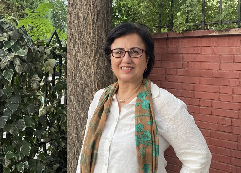 A woman smiles in front of a tree trunk and brick wall.