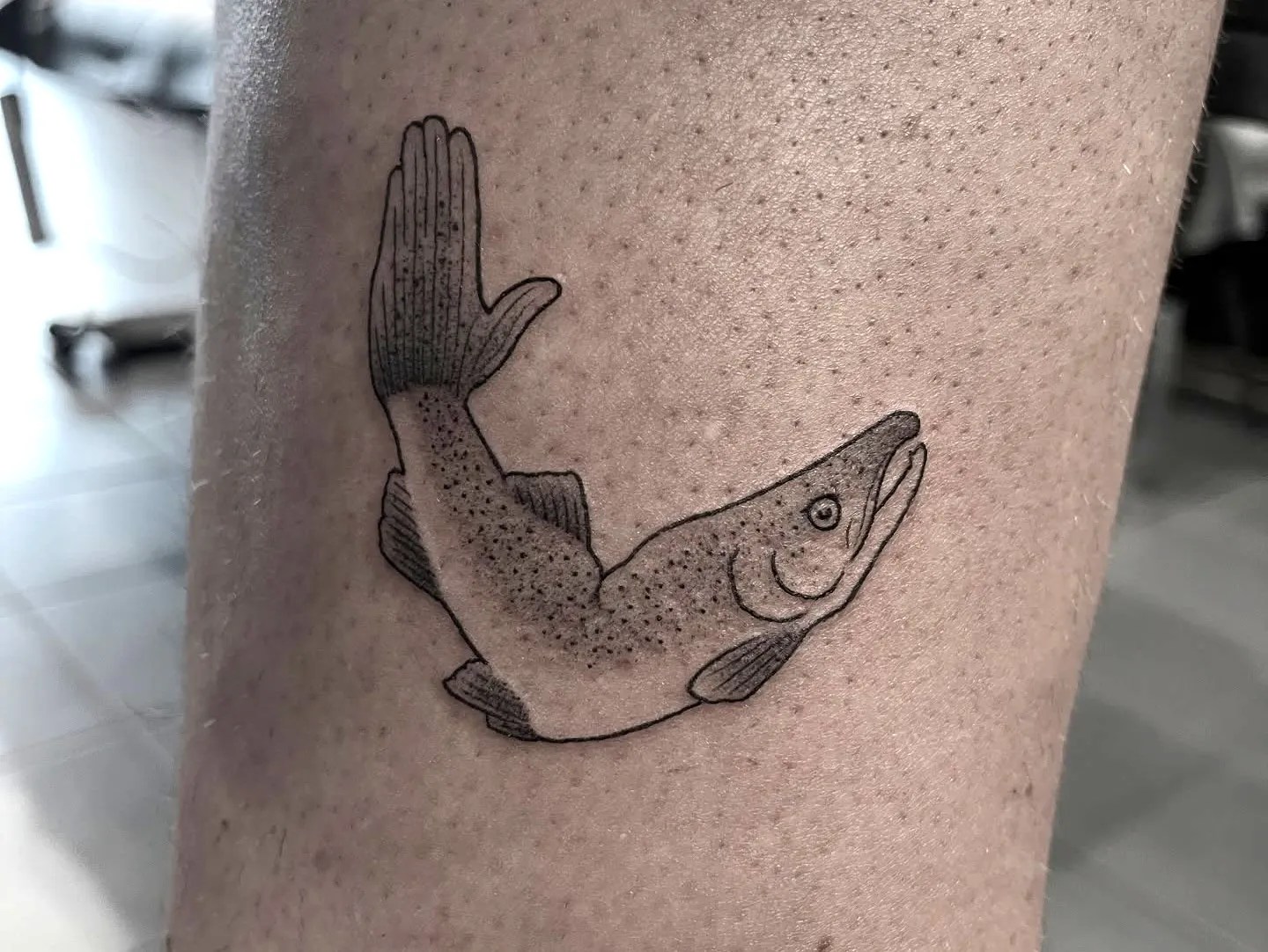 A tattoo of a salmon with an arm instead of a tail.