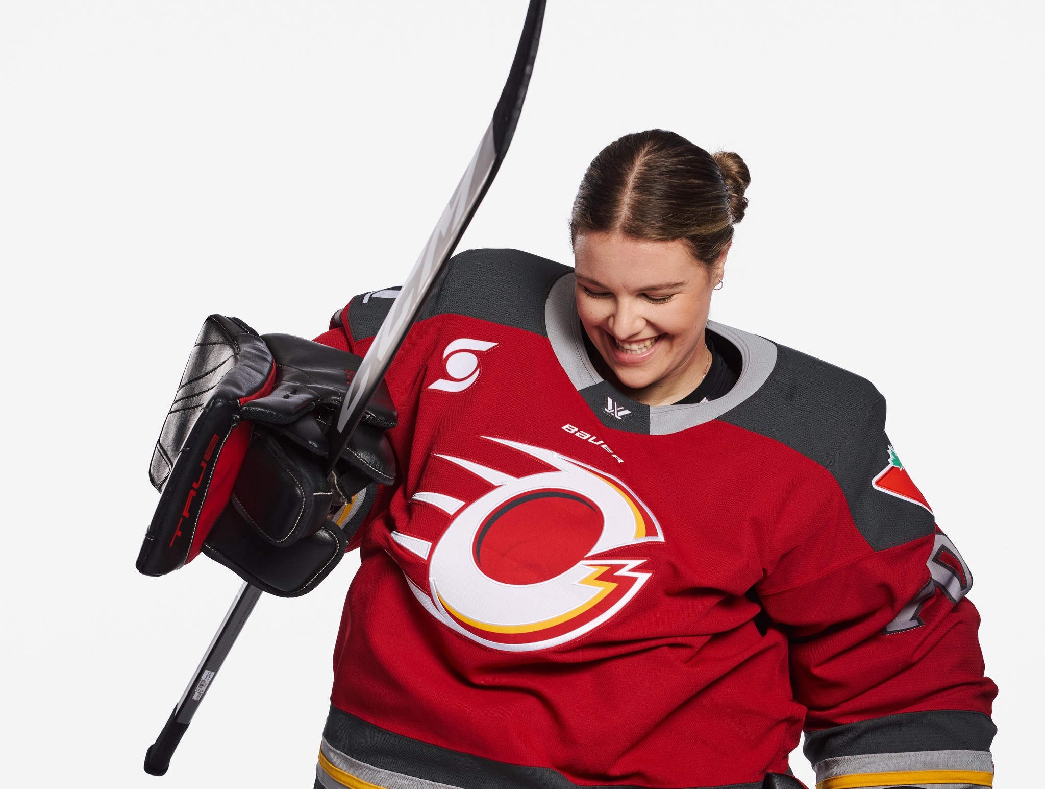 A goalie in a red uniform holds up a stick smiling.