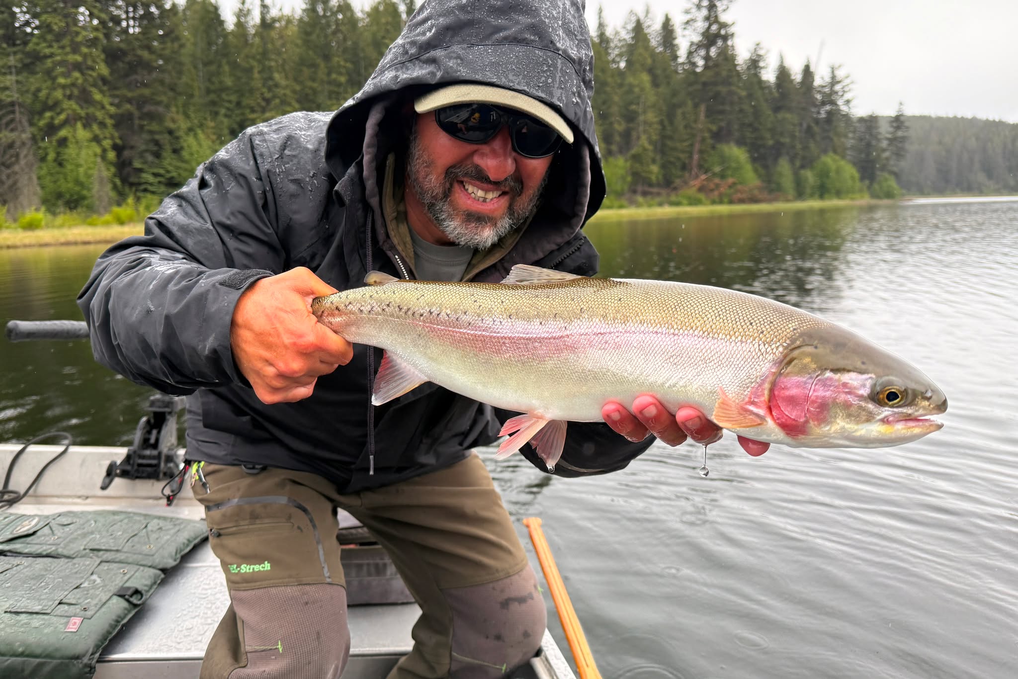A man standing in a boat holds up a trout.