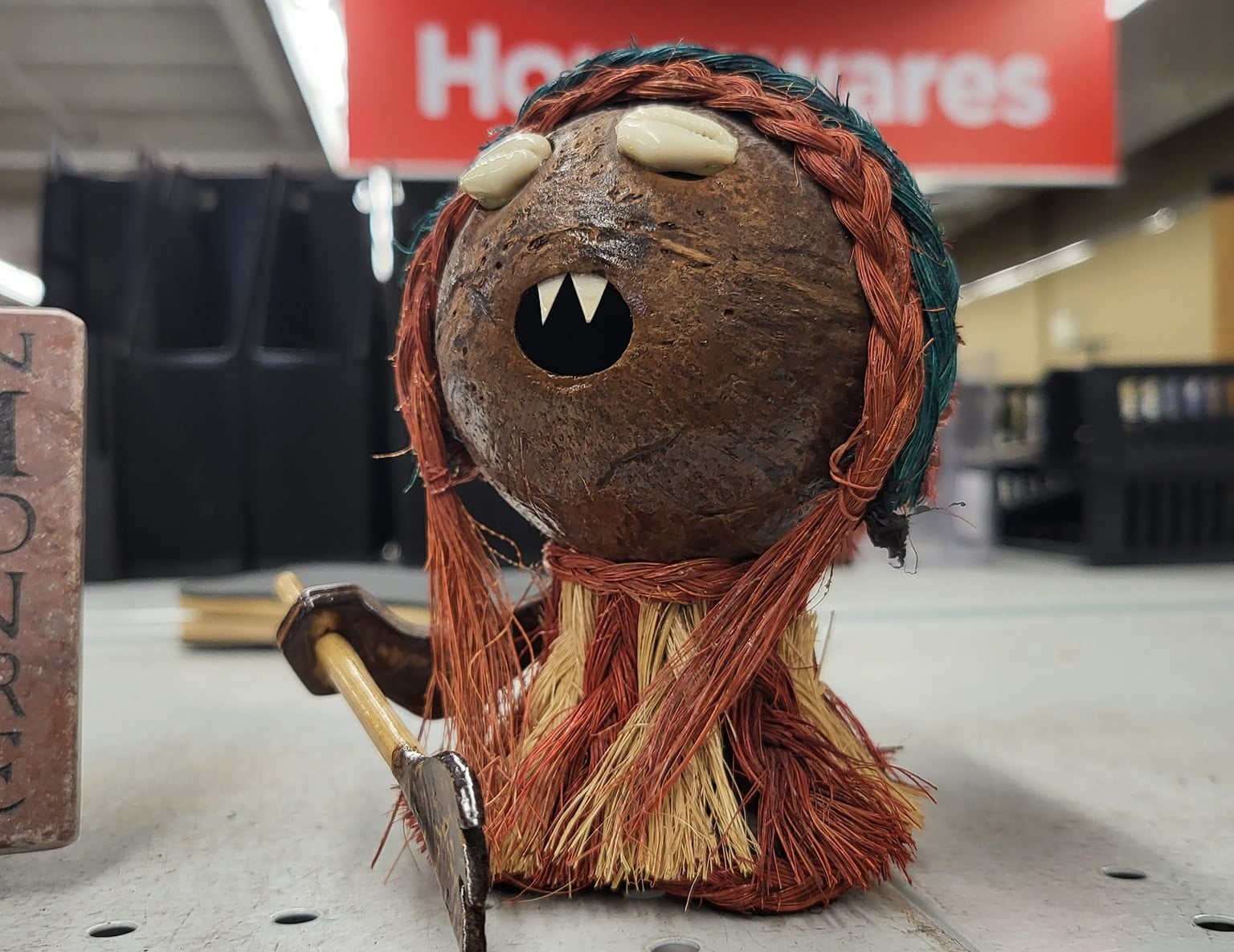 A tiny, bizarre figurine with a coconut head holds a toy axe.