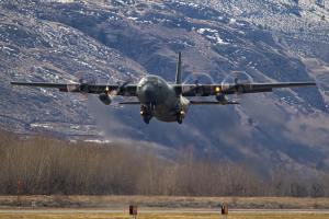 A military airplane is in the air just above a runway.