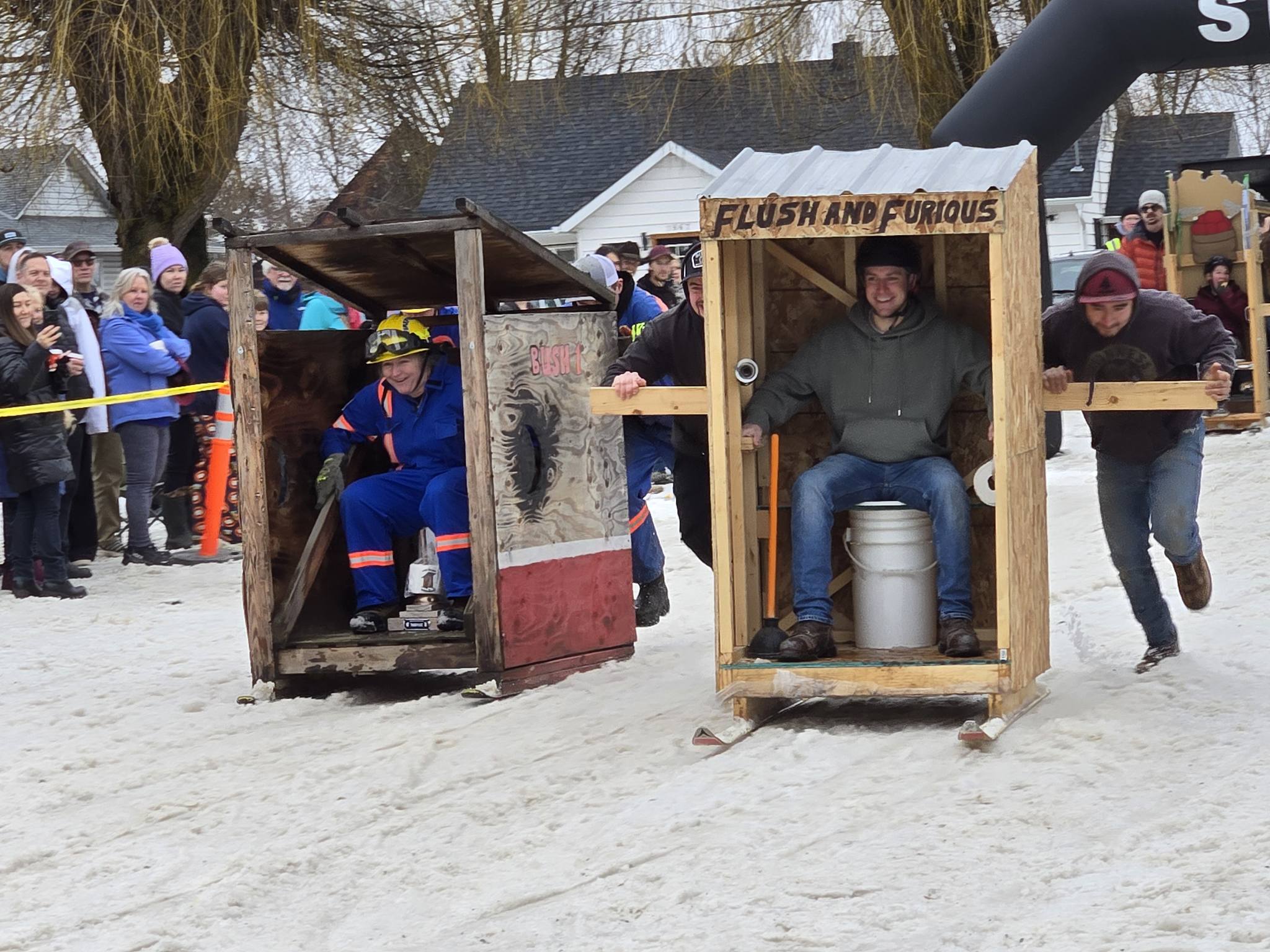 Two teams pushing outhouses on skis.