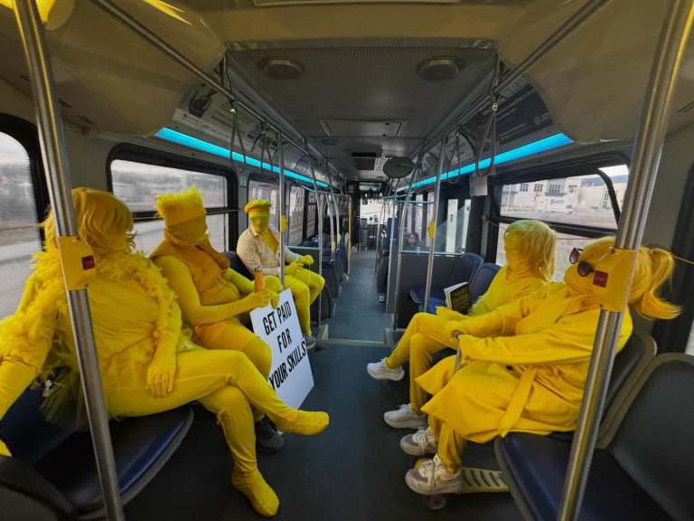 People in yellow morph suits on a bus.
