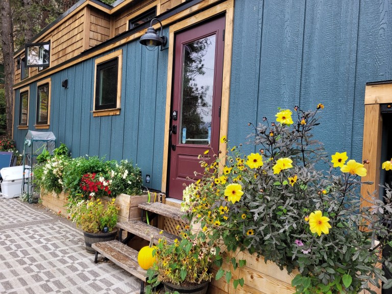 A front of tiny home has flowers blooming in pots around it.
