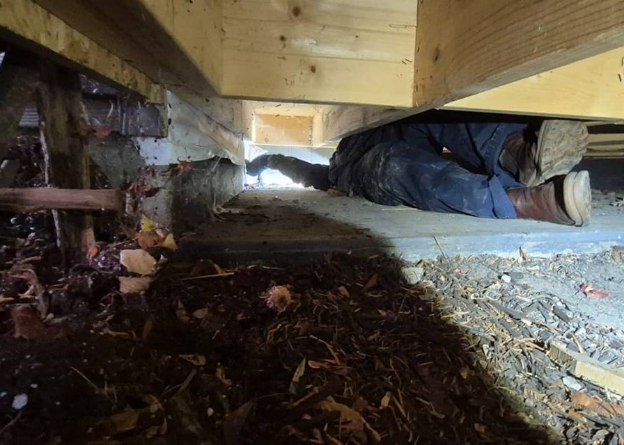 A man in coveralls is stretched out under a porch.