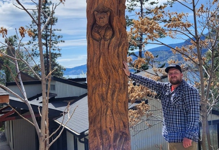 A man stands next to a carved tree.