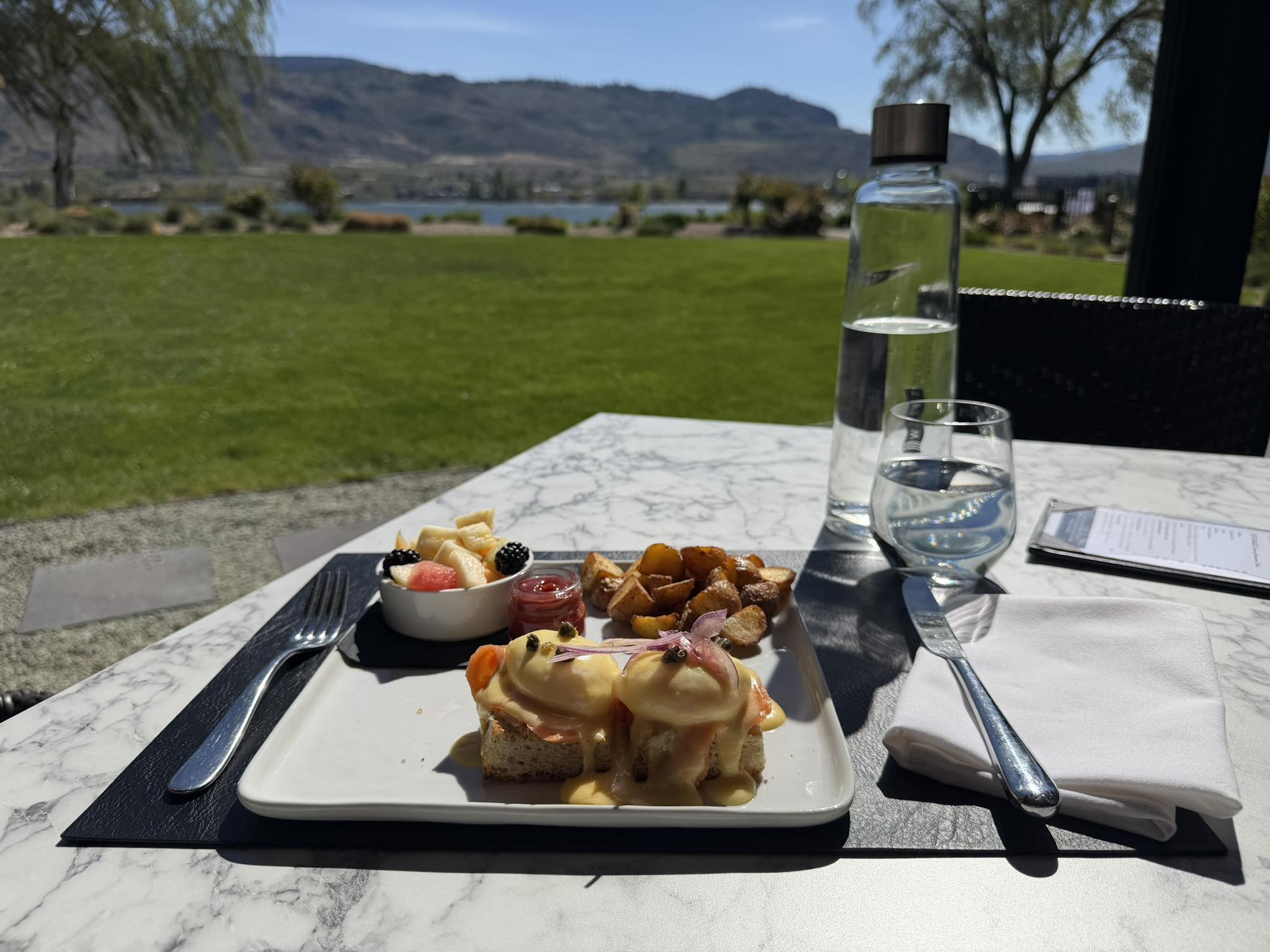 A plate of eggs benedict is shown with a view of a beach.