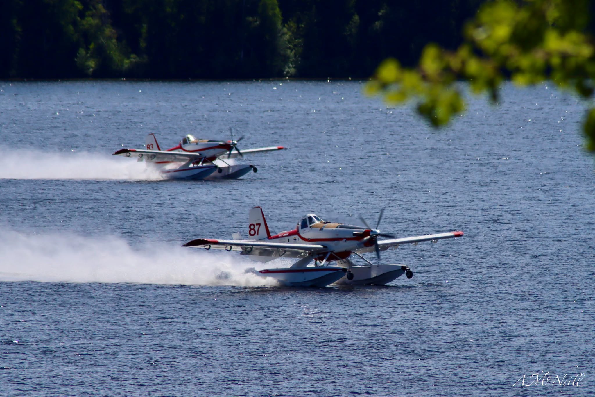 Two skimmer aircraft fill water tanks on a lake.
