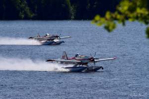 Two skimmer aircraft fill water tanks on a lake.