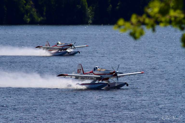 Two skimmer aircraft fill water tanks on a lake.