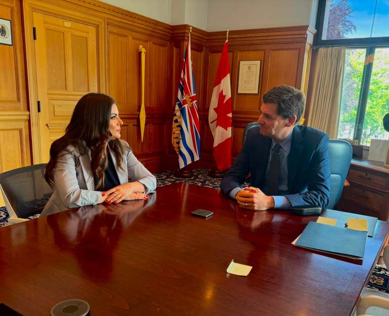 Amelia Boultbee and David Eby sit at a boardroom table.