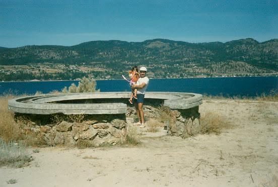 A man in holds a child on sandy land in an old photo.