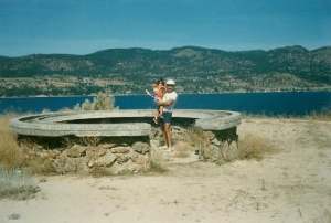 A man in holds a child on sandy land in an old photo.