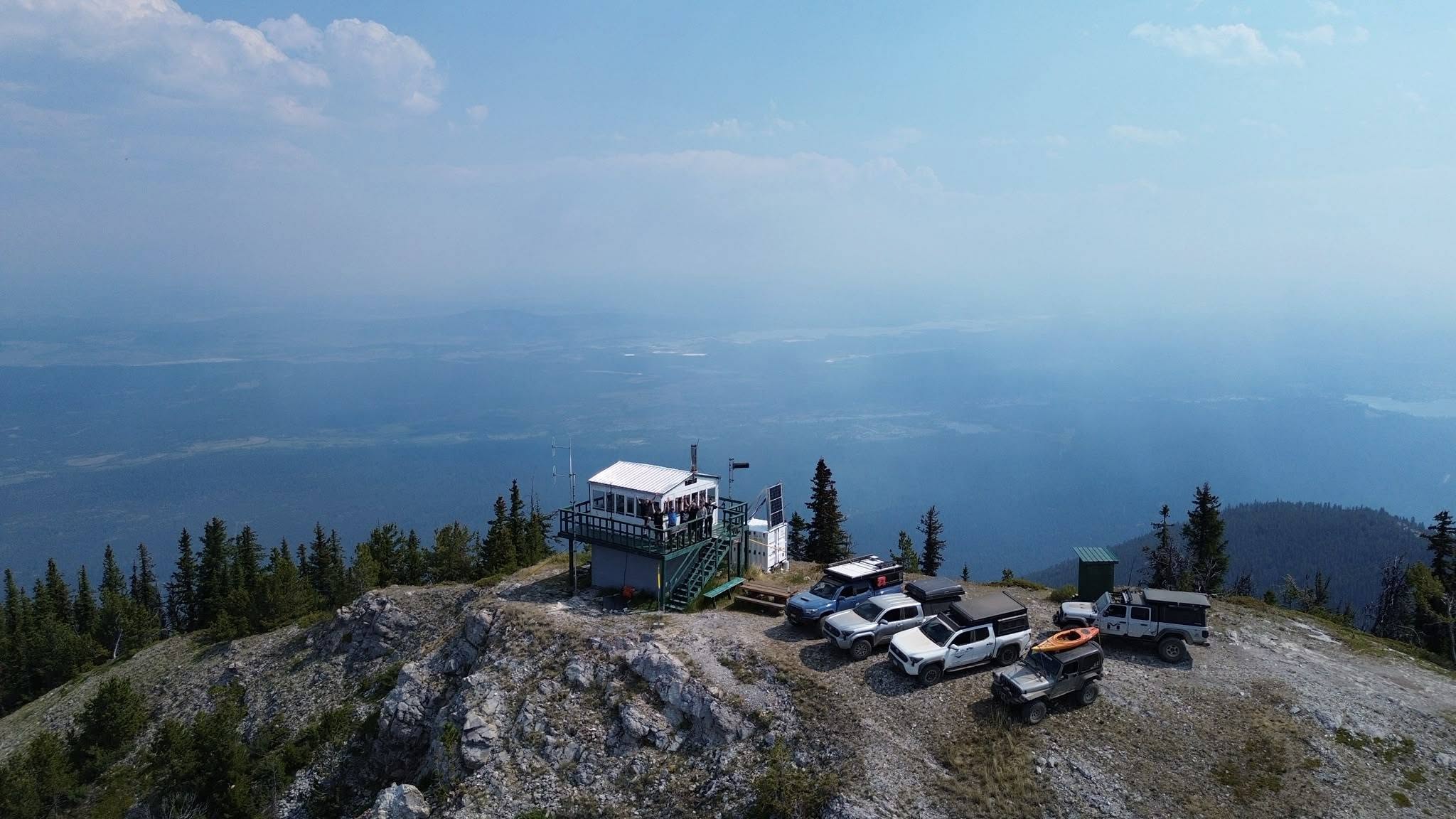A fire tower and Jeeps are on a peak with a panoramic view.