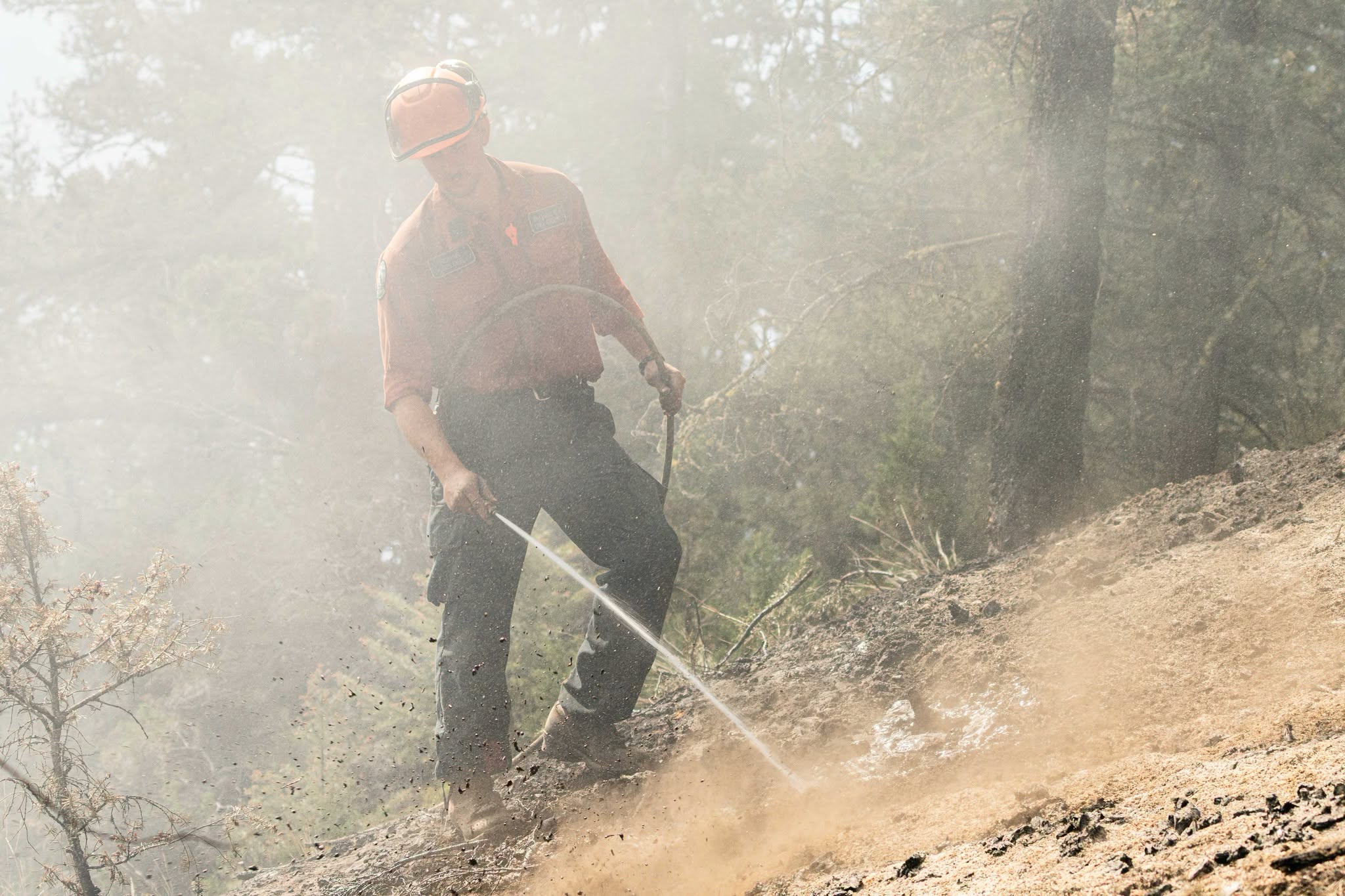 A wildland firefighter putting out a hotspot with a water hose.
