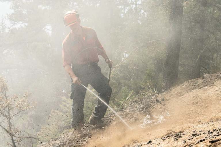 A wildland firefighter putting out a hotspot with a water hose.