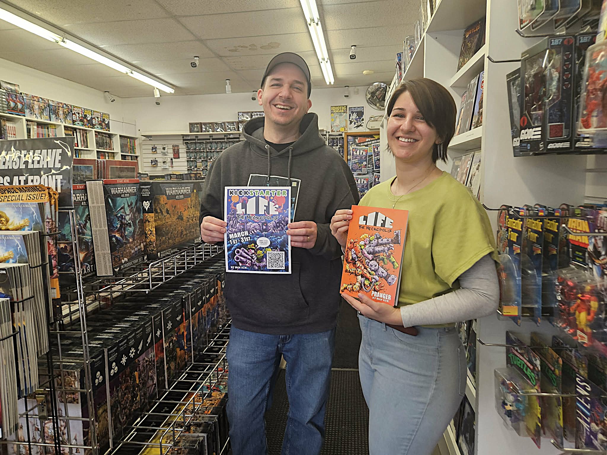 A man and woman stand in a comic book store each holding up a comic book.