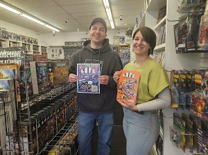 A man and woman stand in a comic book store each holding up a comic book.