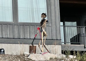 A skeleton decoration has a toque and scarf and is set up to look like its chopping wood.