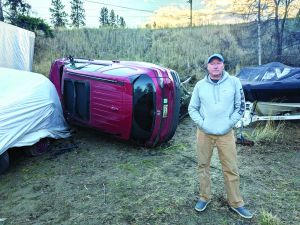 A man stands in front of a vehicle on its side.
