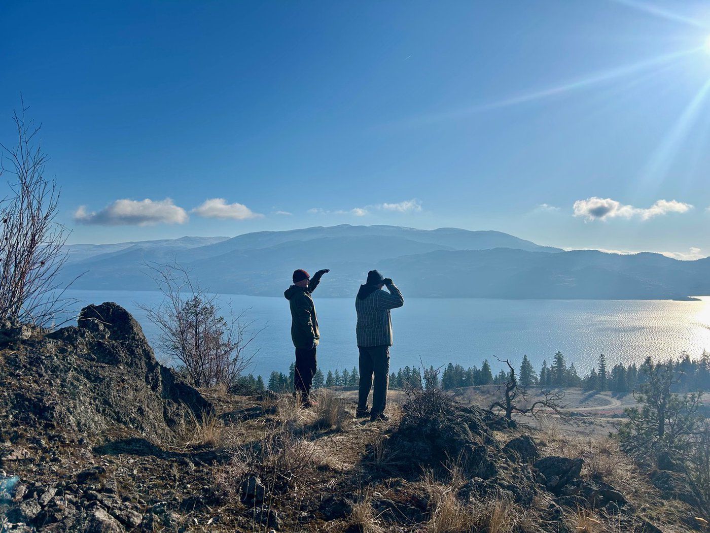 Two people standing on a high overlooking a lake on a sunny day.