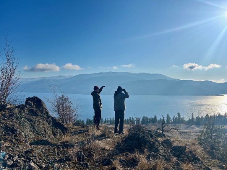 Two people standing on a high overlooking a lake on a sunny day.