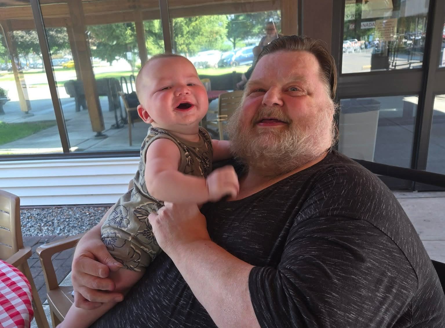 A middle-aged man is smiling while holding up a baby.