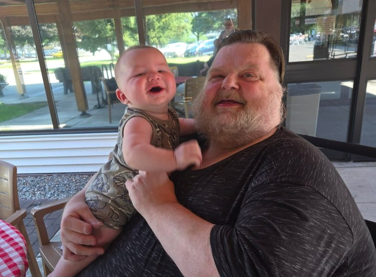 A middle-aged man is smiling while holding up a baby.