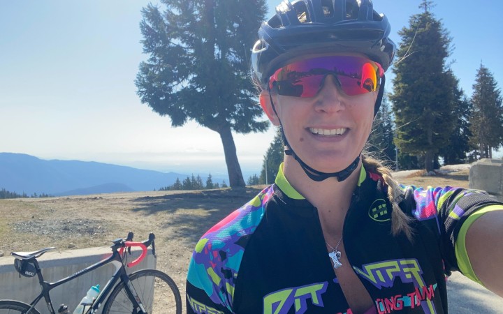 A female cyclist with a bike and mountains in background.