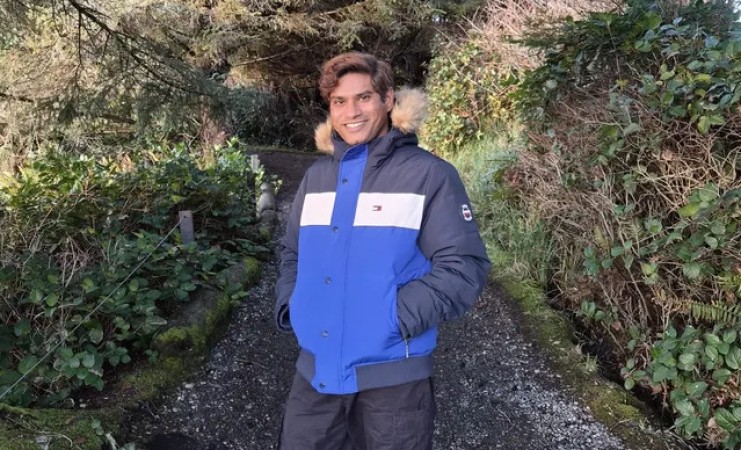 A man stands on a gravel path in a forest.