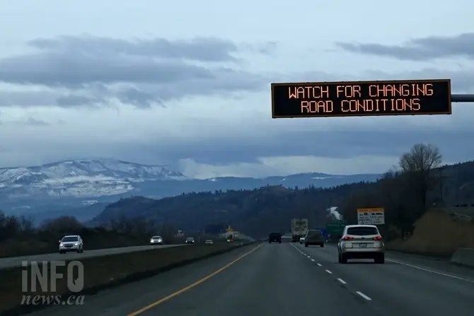 Vehicles on a highway with mountains in the background and a sign warning of changing conditions.