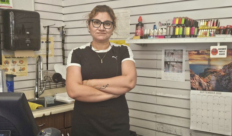 A woman stands behind a counter with her arms crossed.