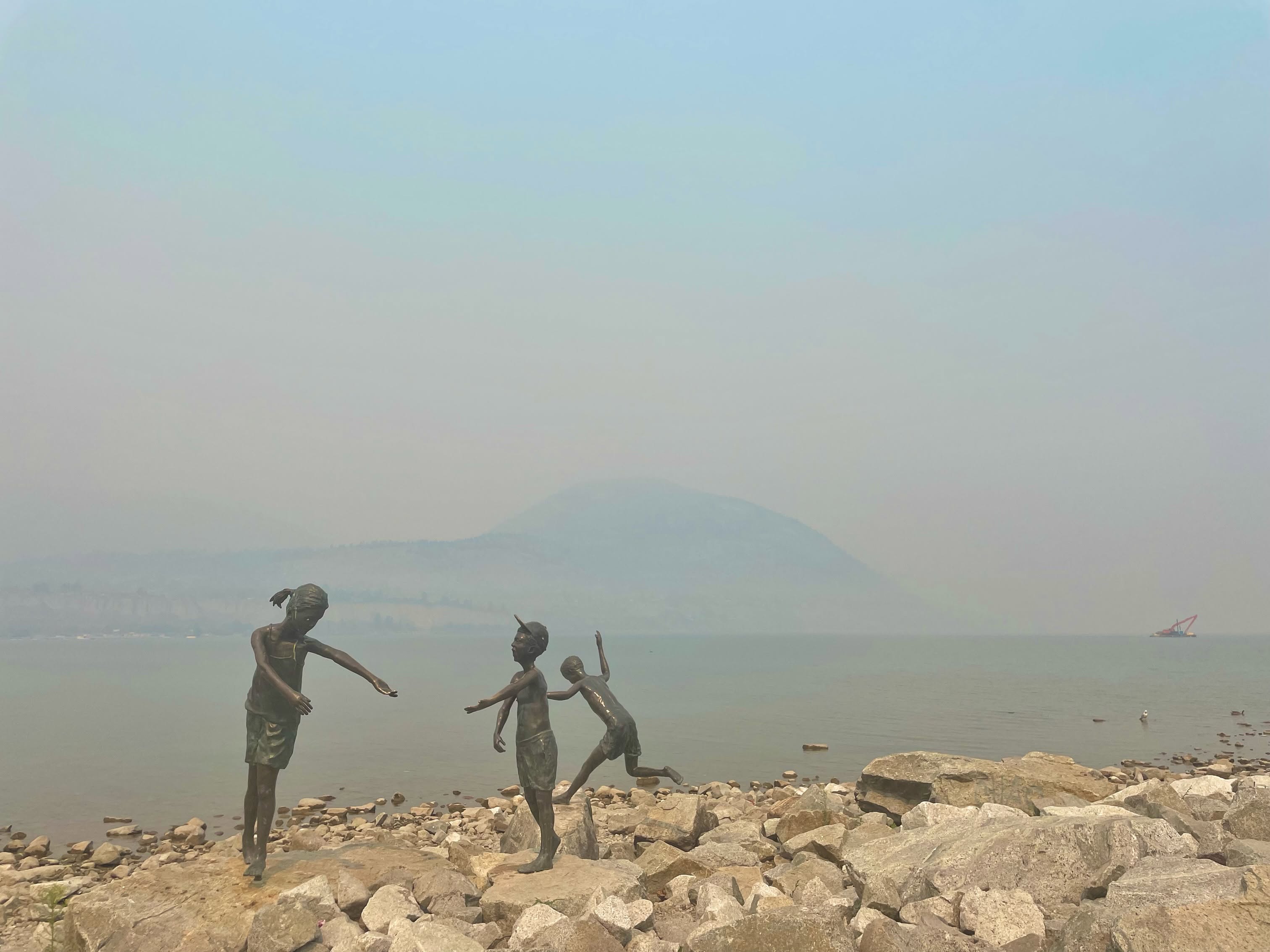 Wildfire smoke settles around statues on a beach.