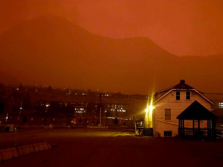 Buildings are seen in the red haze of wildfire smoke.