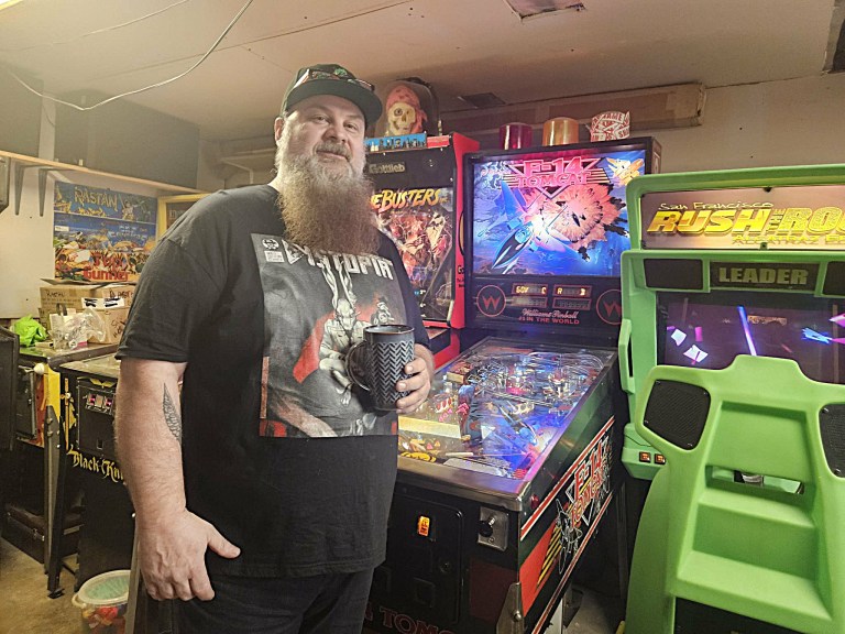 A man stands in front of a pinball machine in a garage.