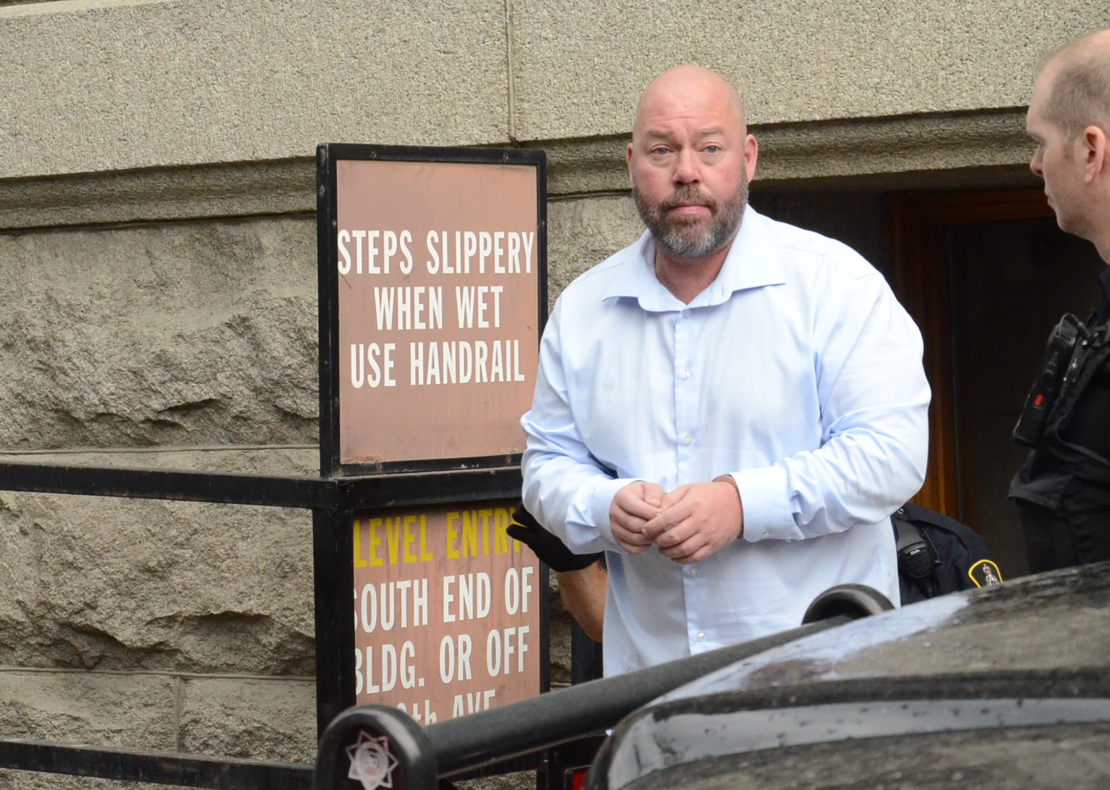 a man in a white shirt and handcuffs walks out of the vernon courthouse.