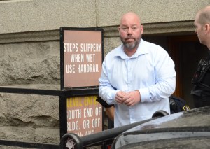 a man in a white shirt and handcuffs walks out of the vernon courthouse.