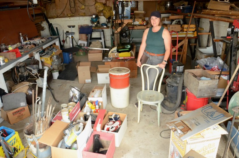 A woman stands in a garage surrounded by boxes of belongings.