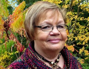 A senior woman wearing glasses and short hair is pictured smiling.